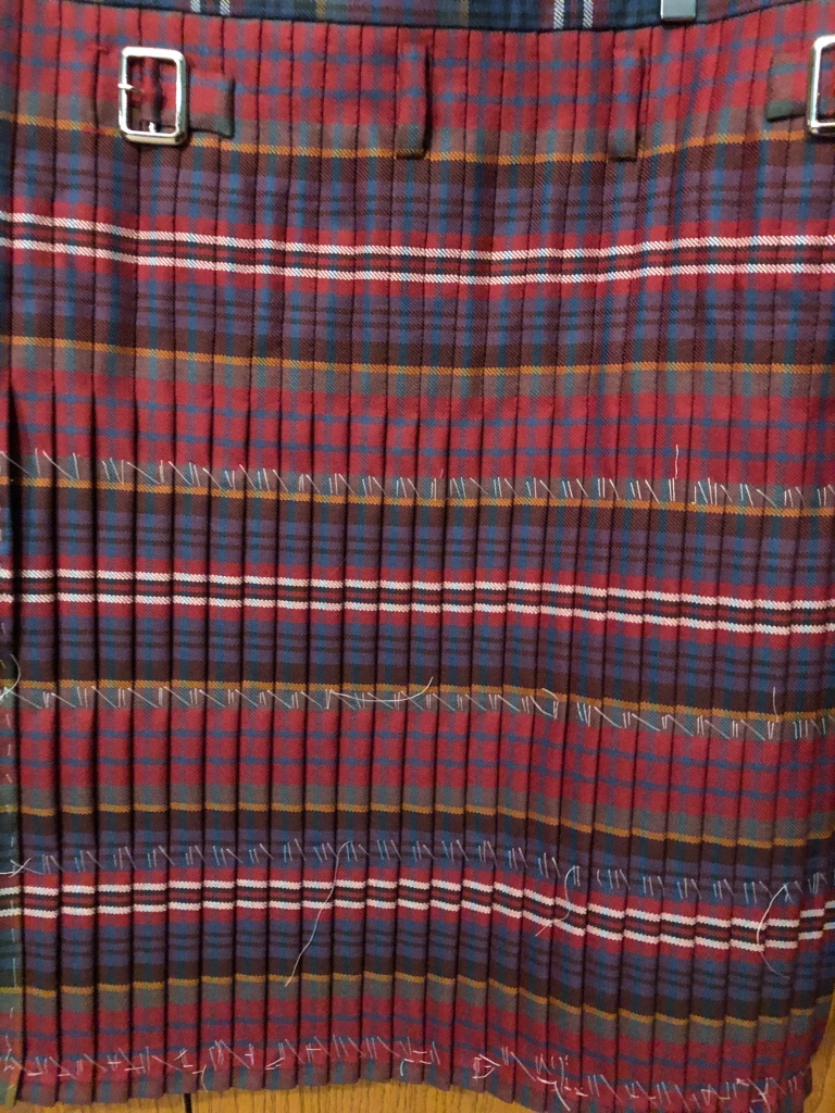 A kilt in MacPherson red muted from the back showing pleats pleated to the first teal stripe